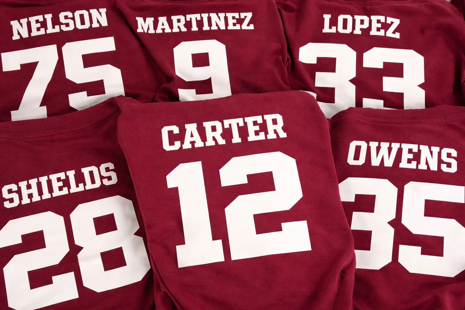 Maroon t-shirts with white text and numbers on a matching background
