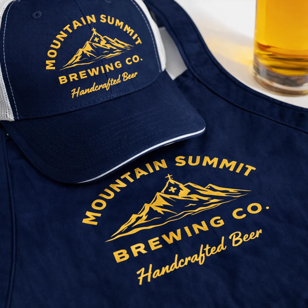 Navy blue cap and t-shirt with 'Mountain Summit Brewing Co.' logo, glass of beer in the background.
