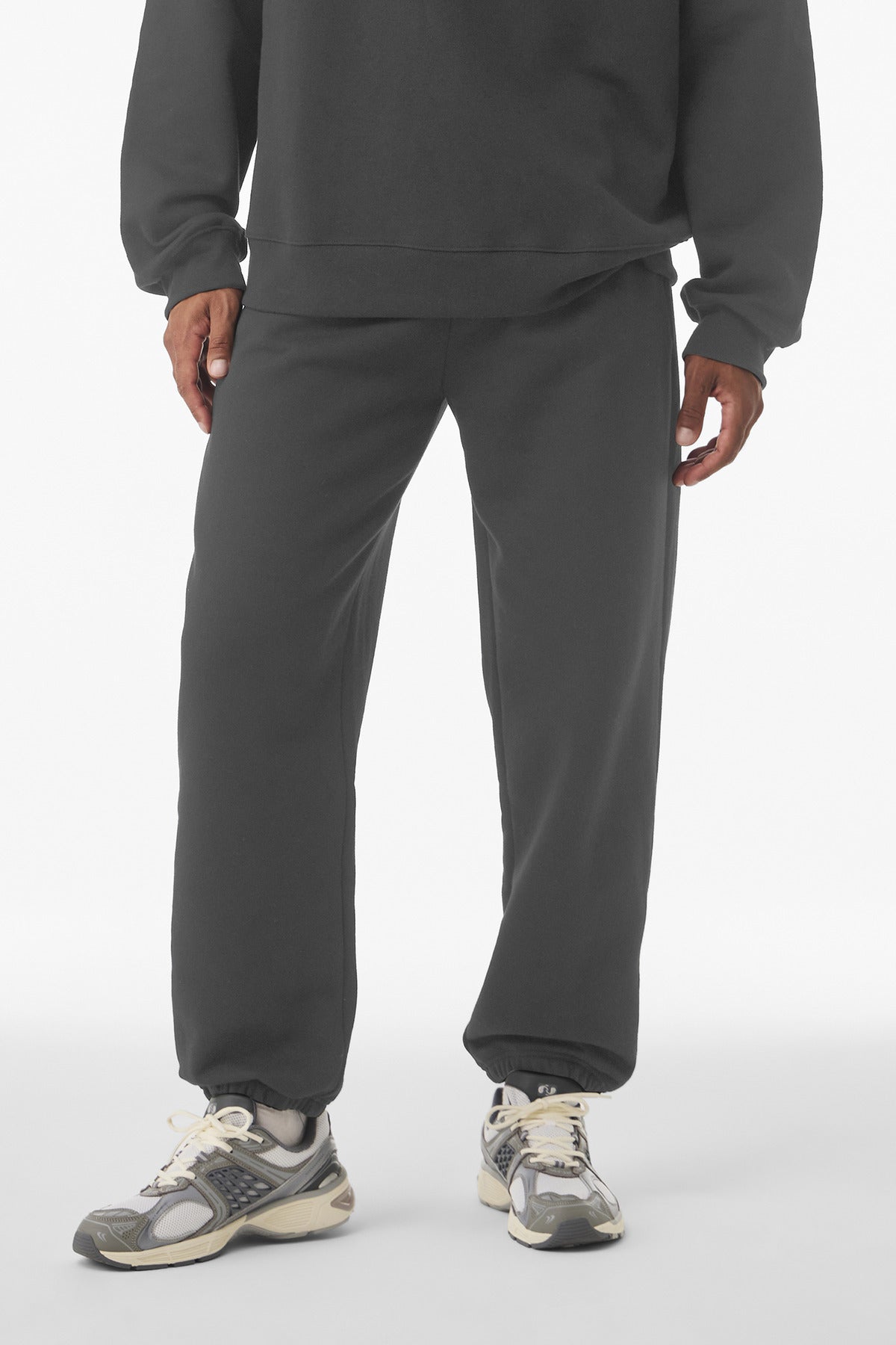 Person wearing a dark gray tracksuit with sneakers on a white background