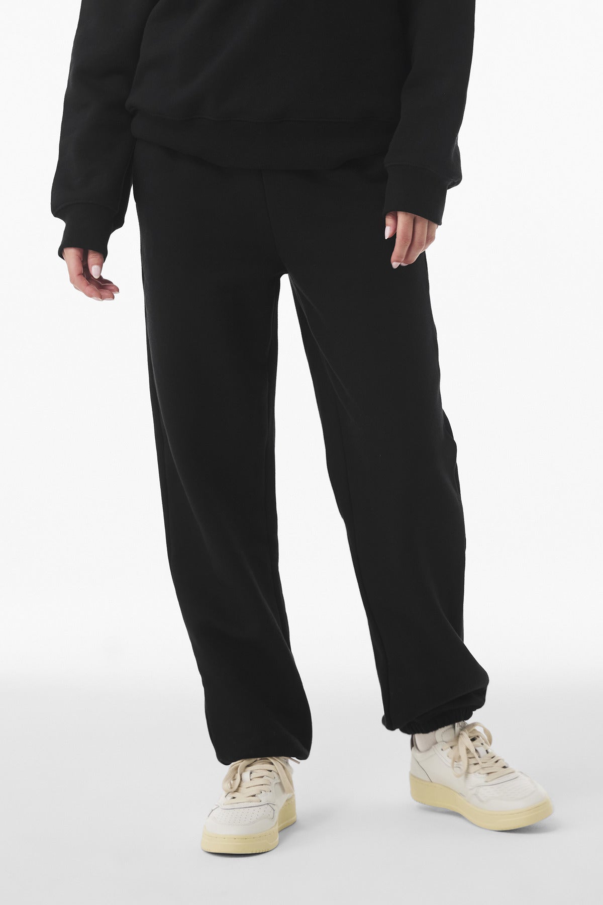 Person wearing black pants and beige sneakers on a white background