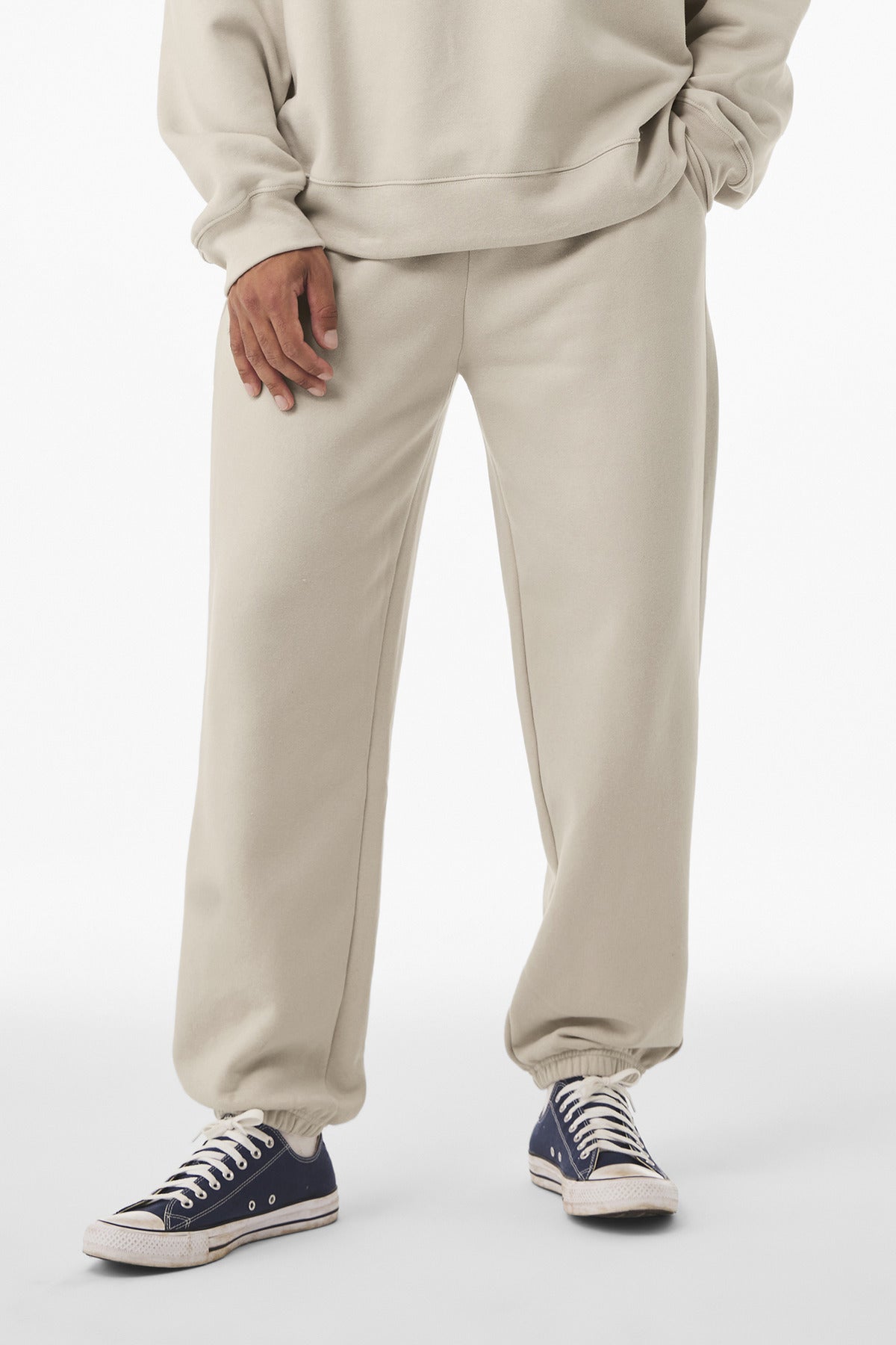 Person wearing a beige tracksuit with navy sneakers on a white background